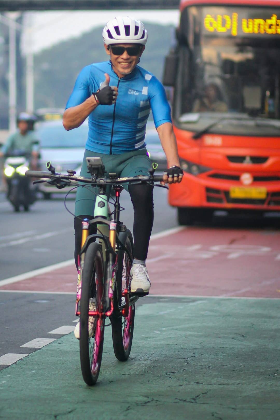 Cyclist in blue jersey gives a thumbs-up on a bike lane.